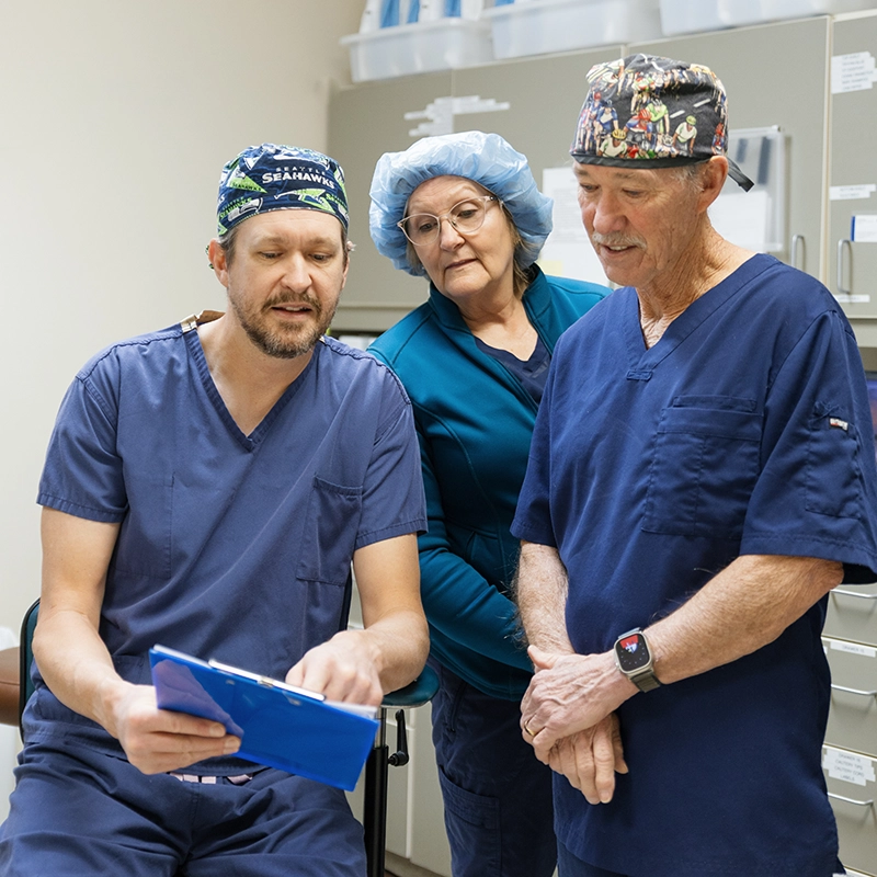 Three medical professionals at The Eye Center in Yakima wearing scrubs reviewing a document on a clipboard in a clinical setting.