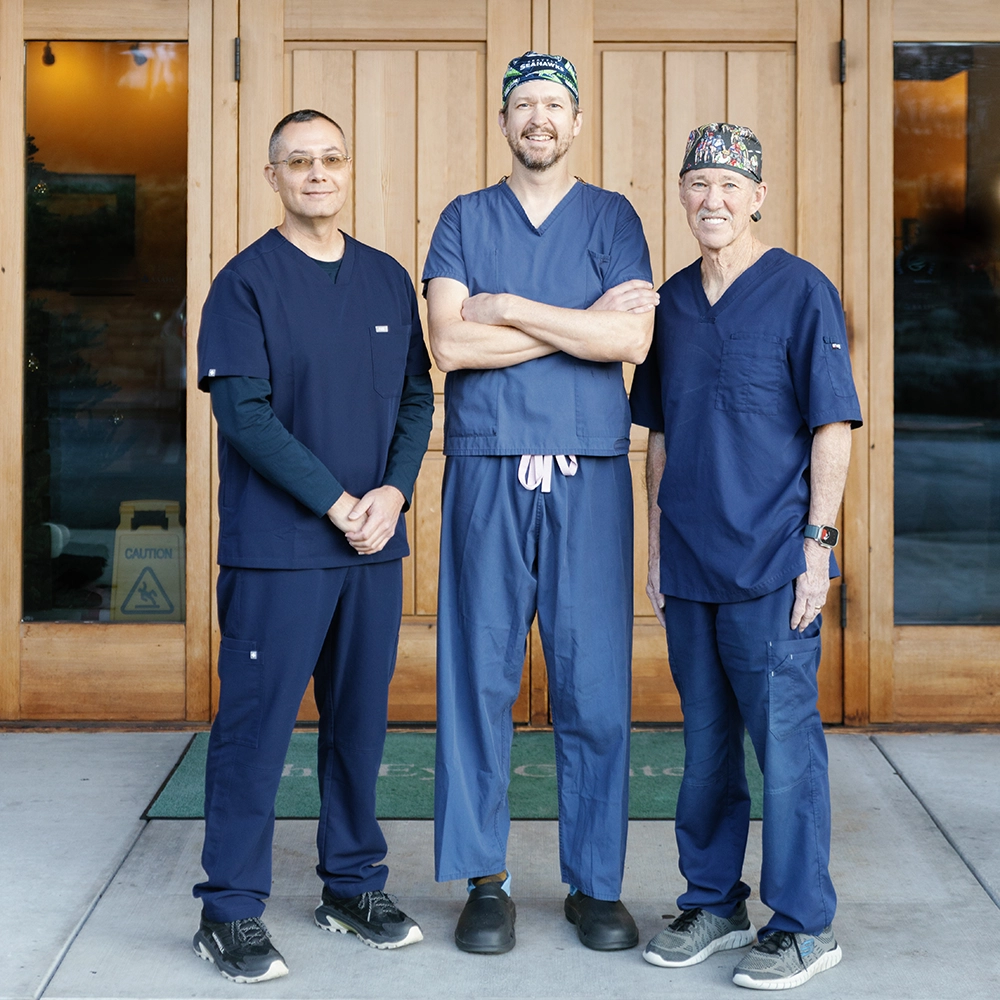 The Eye Center Yakima Building entrance with large wooden double doors, stone pillars, and a wooden overhang roof, surrounded by evergreen trees.