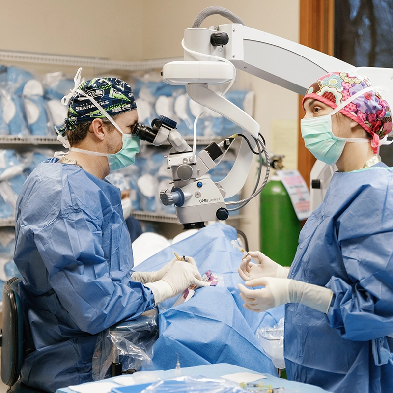 Three medical professionals at The Eye Center in Yakima wearing scrubs and surgical caps discussing notes on a clipboard in a clinical storage room.