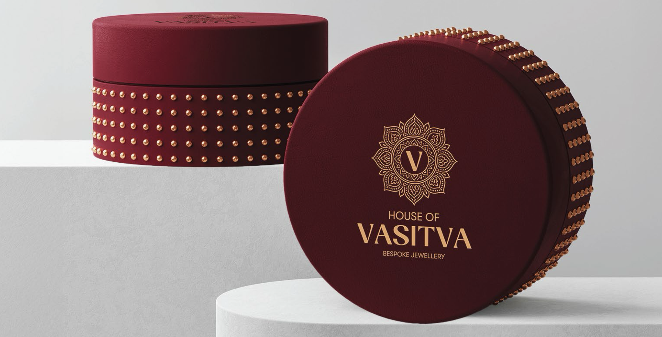 Two round maroon boxes adorned with gold studs and House of VASITVA bespoke jewellery logo on one box.