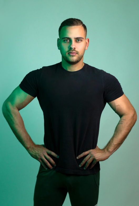 Young muscular man in a black t-shirt standing with hands on hips against a green background.