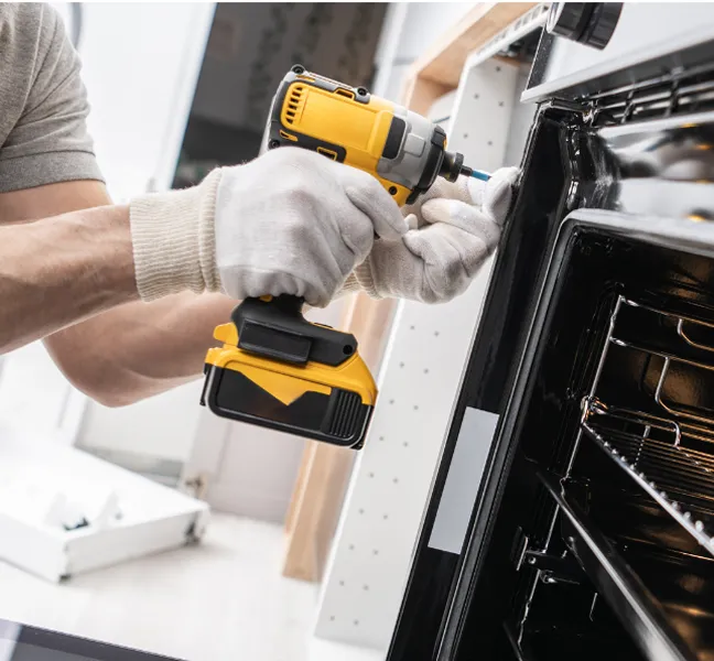 A technician using a yellow cordless power drill to fix or install a household oven.