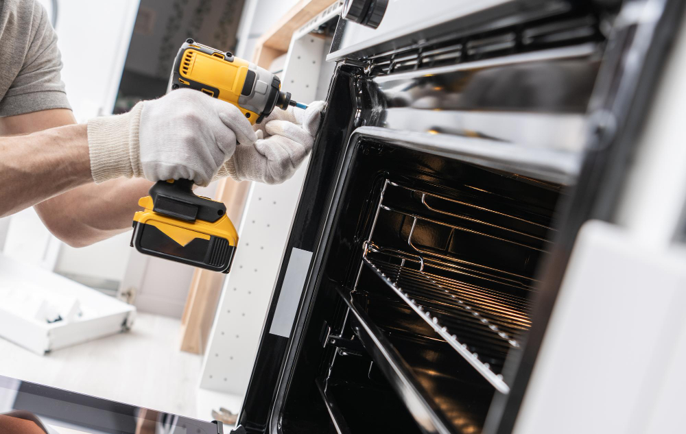 A technician using a yellow cordless power drill to fix or install a household oven.