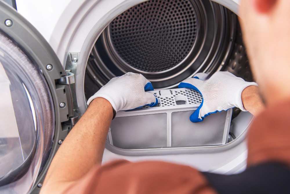 Technician repairing an open dishwasher in a kitchen using a screwdriver.