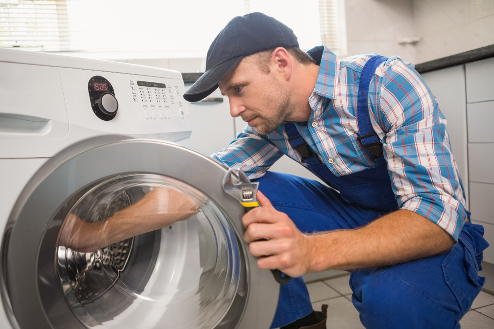 Technician repairing a white front-loading washing machine with an open toolbox on the floor.