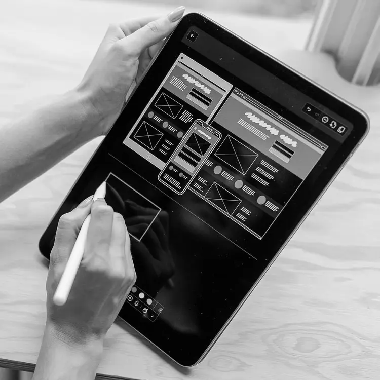 Schwarzweissfoto: Hände skizzieren mit einem Stift Wireframes für Website und App auf einem iPad