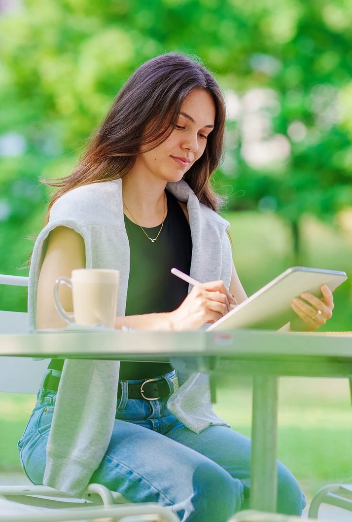 Larissa Sequeira zeichnet ein UX-Design mit einem Stift auf dem iPad, daneben eine Tasse auf einem Gartentisch