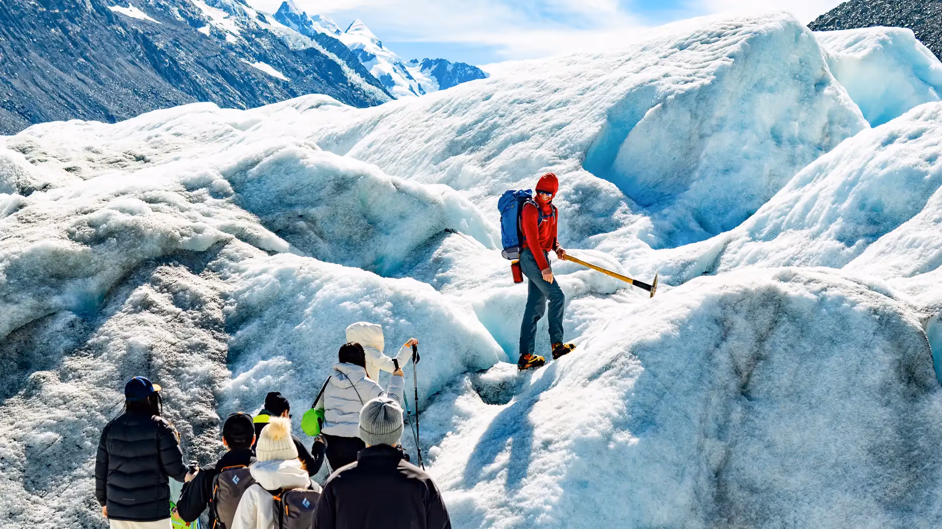 Tasman Glacier Helihike guide cutting steps in ice while guests observe