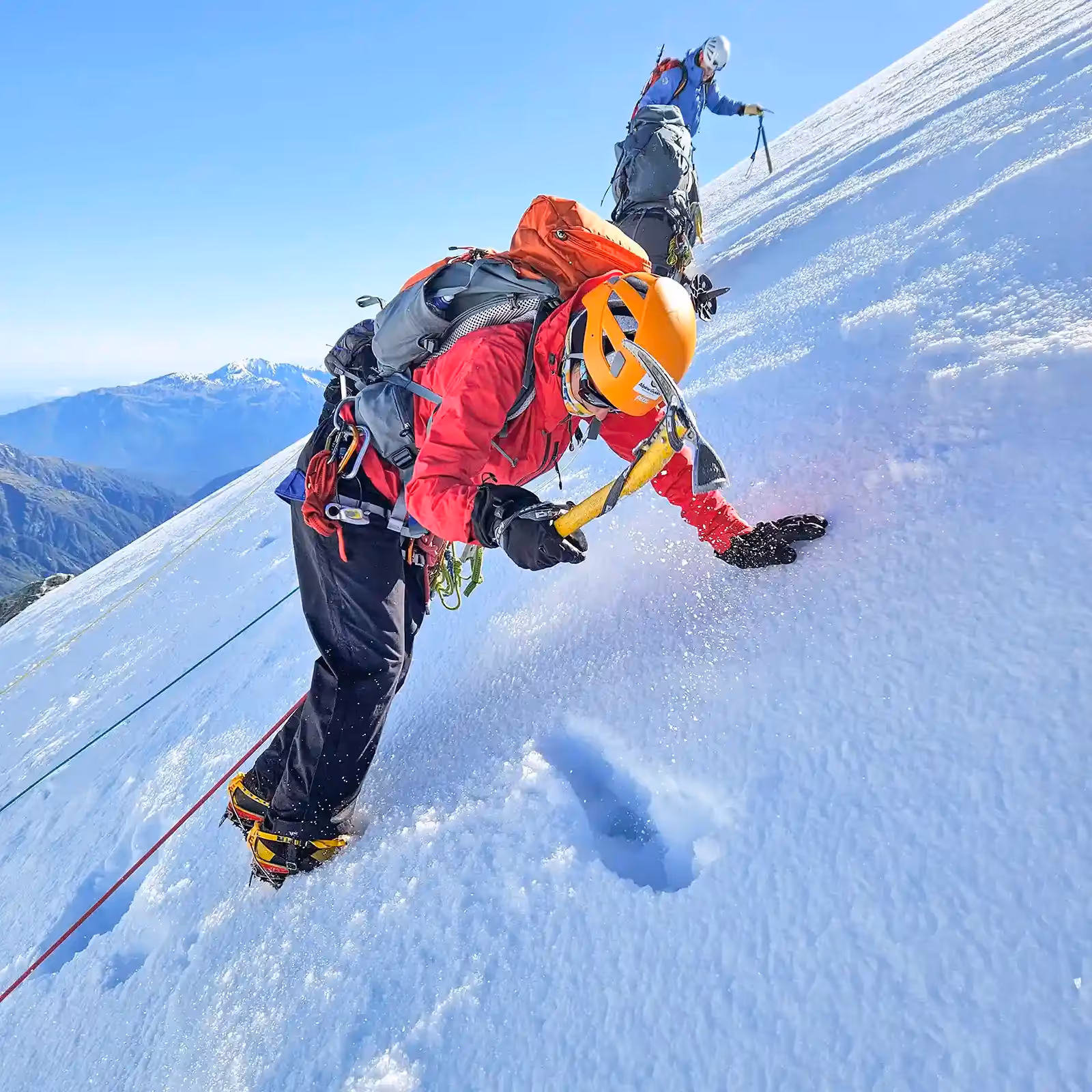 Climbers ascending steep snow and ice using ice axe and crampons