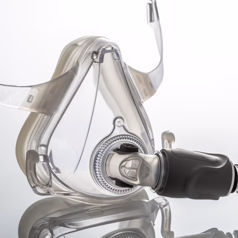 Close-up of a transparent CPAP mask with a black connector on a reflective surface.