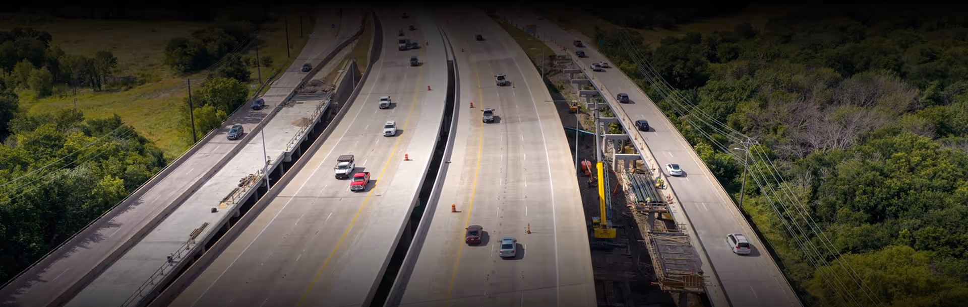 Aerial view of a multi-lane highway with cars and construction work on the right side surrounded by green trees.