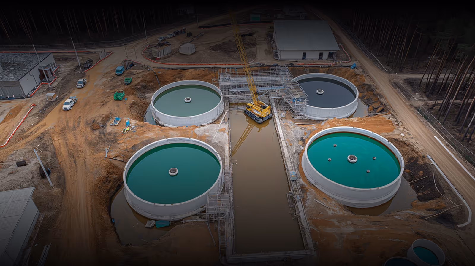 Aerial view of a water treatment facility under construction with large circular tanks filled with water and construction equipment.
