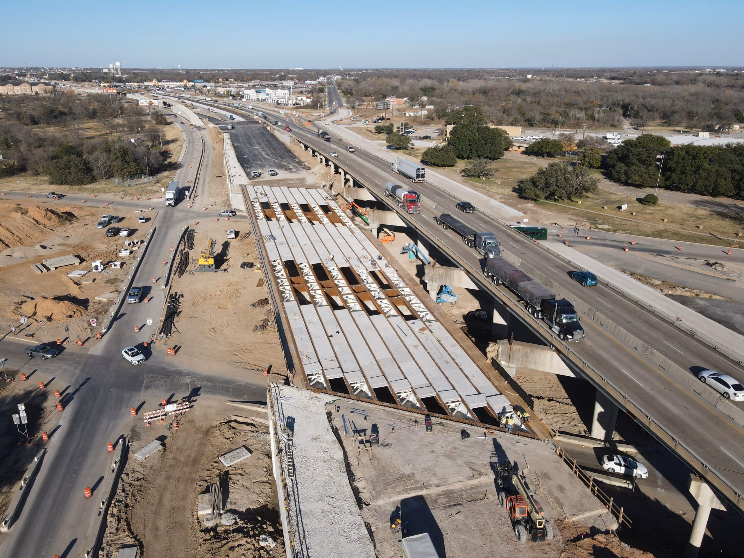 Aerial view of a highway under construction with trucks on the adjacent open road and construction equipment on site.