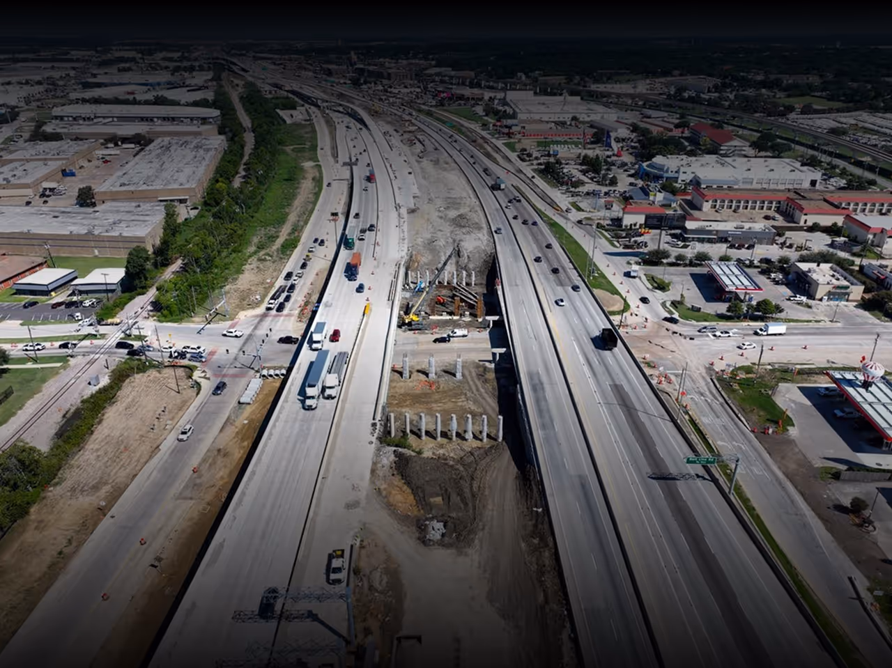 Aerial view of a highway under construction with vehicles driving on both sides and construction equipment in the center.