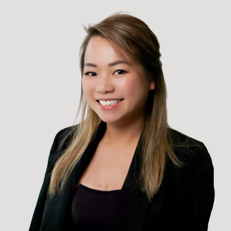 Smiling woman with long light brown hair wearing a black blazer and top against a light background.