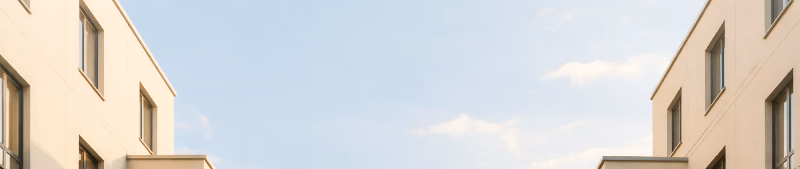 Modern beige building with multiple windows against a partly cloudy blue sky.