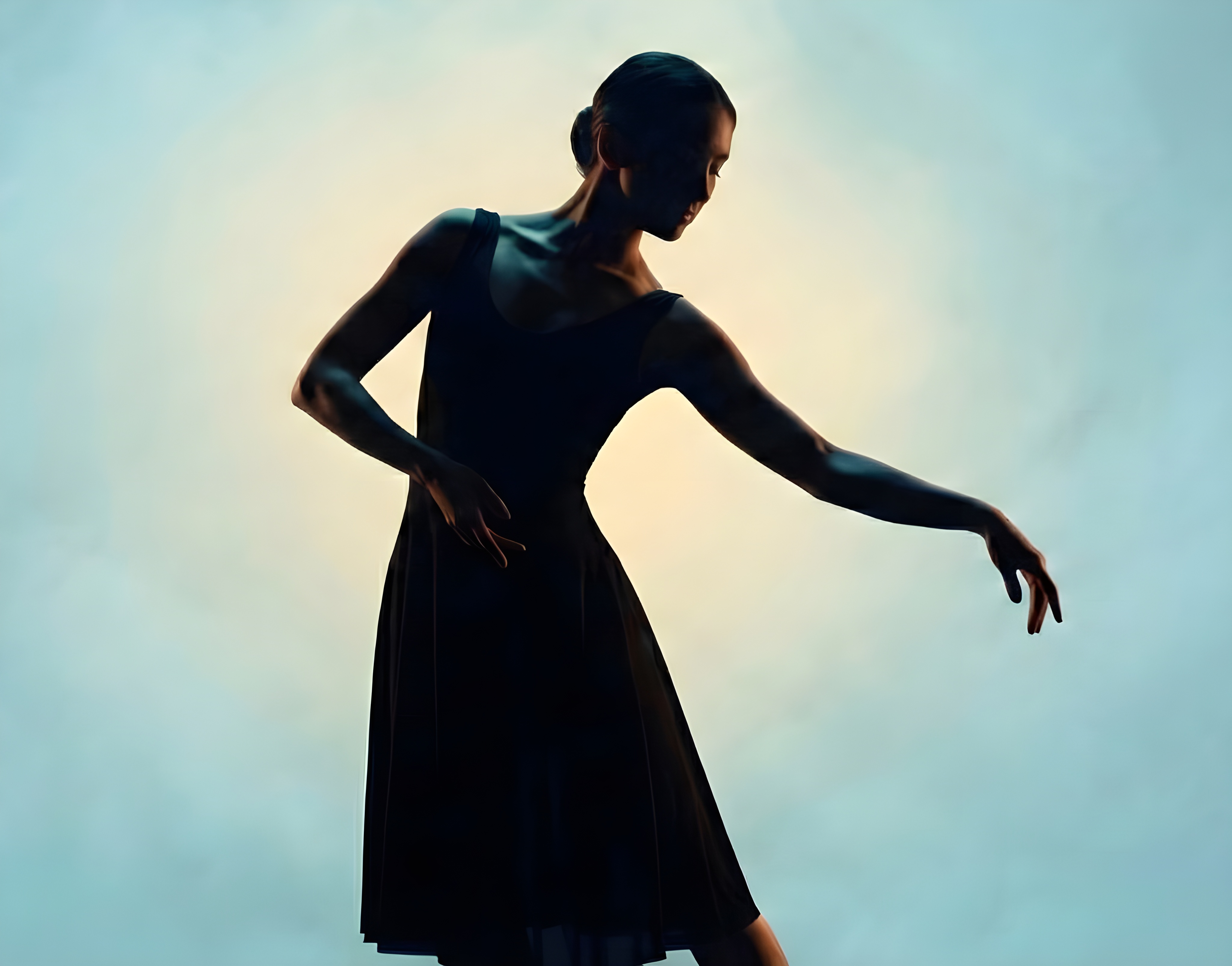 Silhouette of a ballerina in a black dress gracefully posed against a soft gradient background.