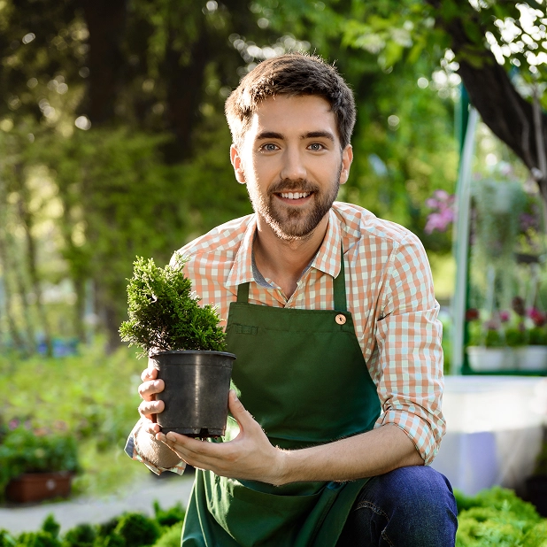 Smiling nursery owner holding a healthy potted plant, representing successful small-scale farming