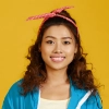 Smiling woman with curly hair wearing a blue jacket and red headband on a yellow background.
