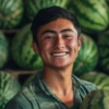 Smiling young man with short dark hair standing in front of stacked watermelons.