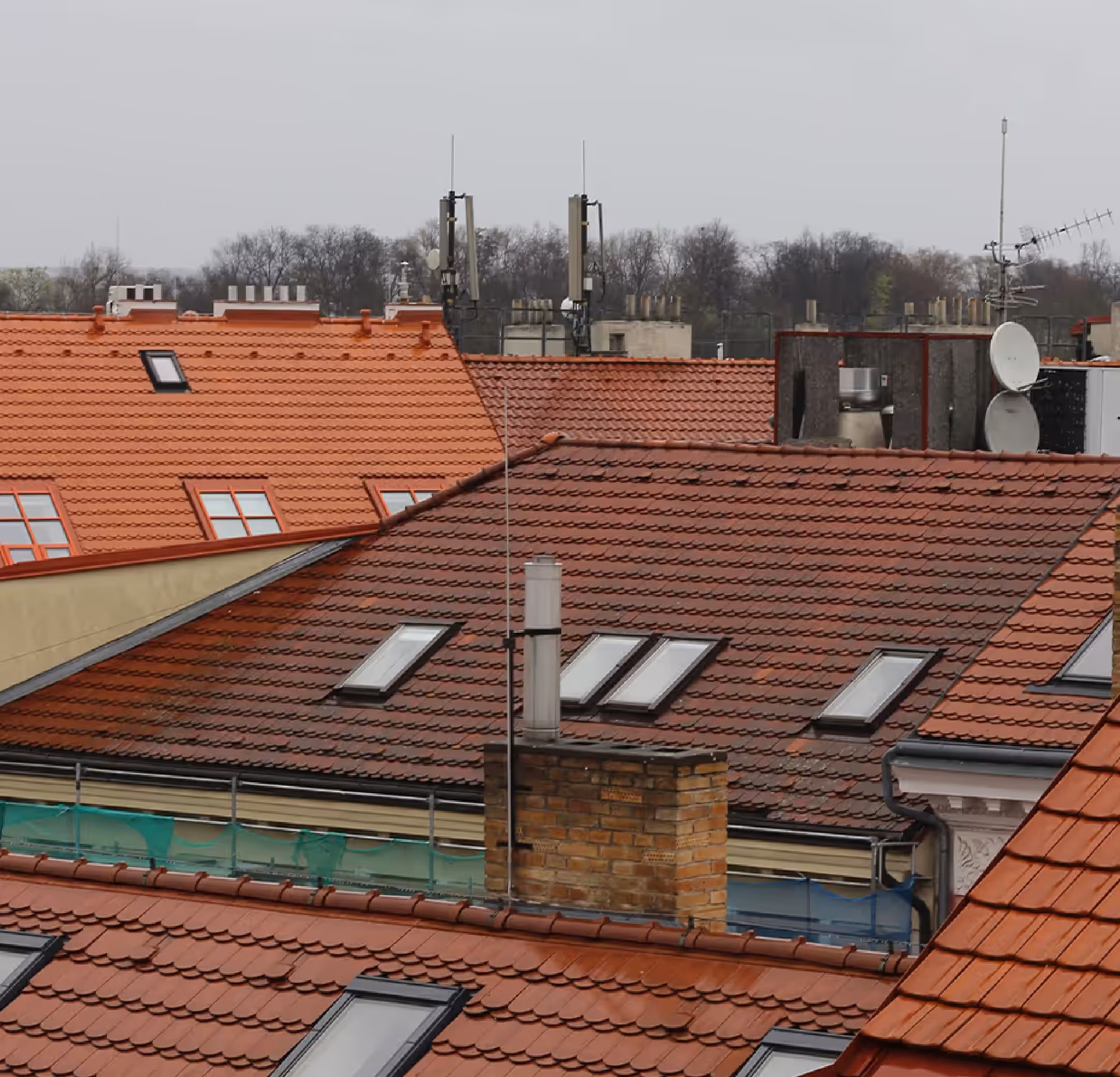 View of red-tiled rooftops with skylights and chimneys under an overcast sky.