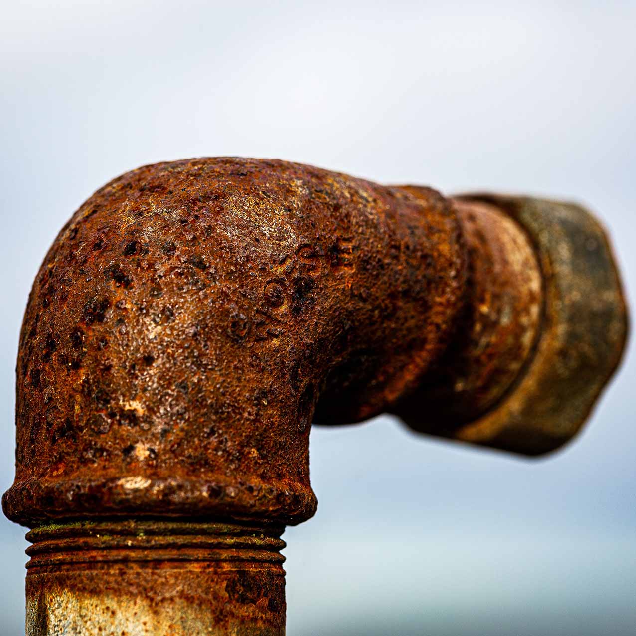 Visible corrosion on pipes; plumbing in north Georgia. Close-up view of rusted pipe, with sky in background.