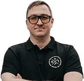 Keskellä seisova mies mustassa poolopaidassa, jossa on logo, taustalla sumuinen maisema ja liikennemerkkejä.