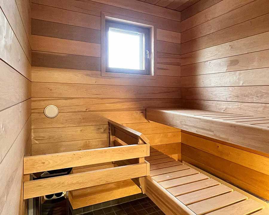 Puinen sauna, jossa on penkit, pieni ikkuna ja puupanelointi seinillä ja katossa. Valoisa ja lämmin tunnelma.