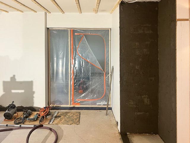 Sisätila, jossa on työkaluja lattialla, muovilla peitetty oviaukko ja tummanruskea seinä.