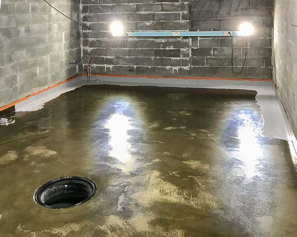 Kellarin betonilattia, jossa on viemäri, seinät ovat harmaita betonitiiliä ja valaistus on kirkas.