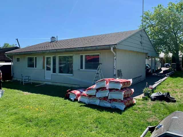 Yksikerroksinen talo, jossa on ruskea katto, valkoinen ulkoverhous ja suuri kasa eristysmateriaalia nurmikolla aurinkoisena päivänä.