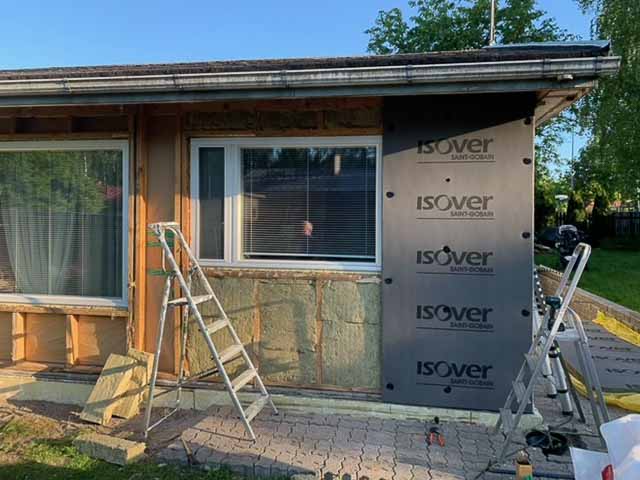 Ulkoseinän remontti, jossa näkyy eristys, Isover-levyjä, kaksi tikapuut ja ikkunat. Valoisa päivä.