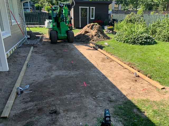 Ulkona on rakennustyömaa, jossa on vihreä traktori, puutavaraa ja maakasa. Valoisa päivä.