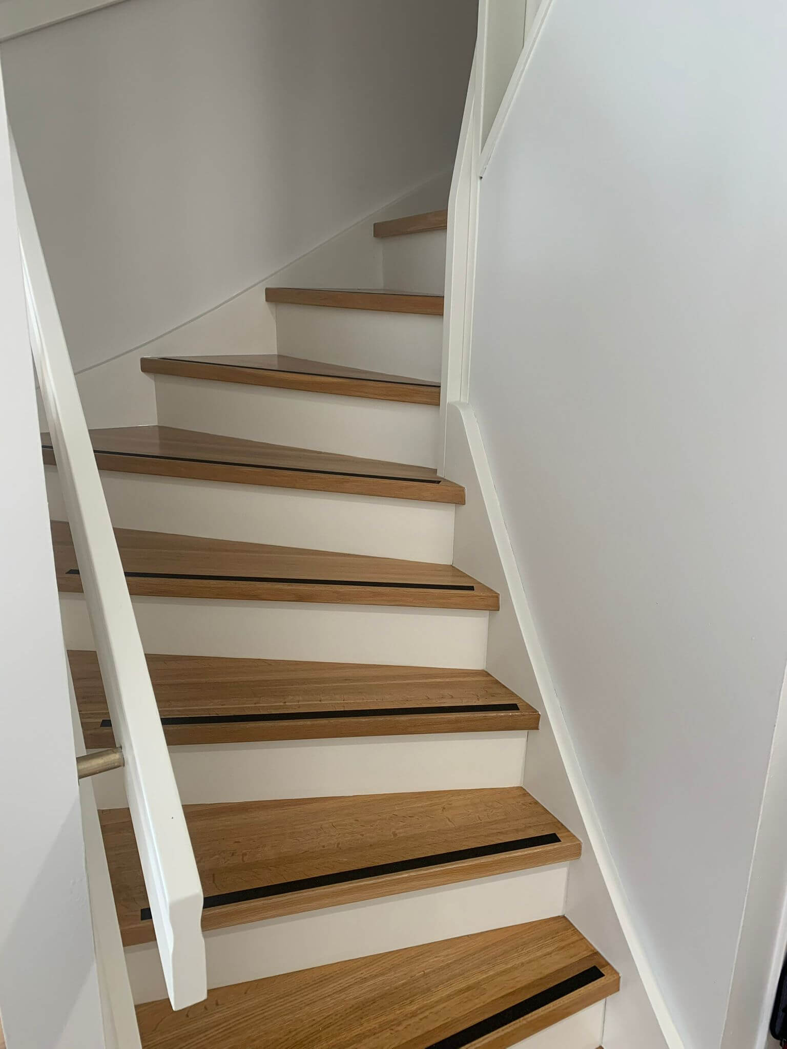 Vaaleat puuportaat, joissa on valkoiset nousut ja mustat liukuesteet, valkoisen kaiteen vieressä.