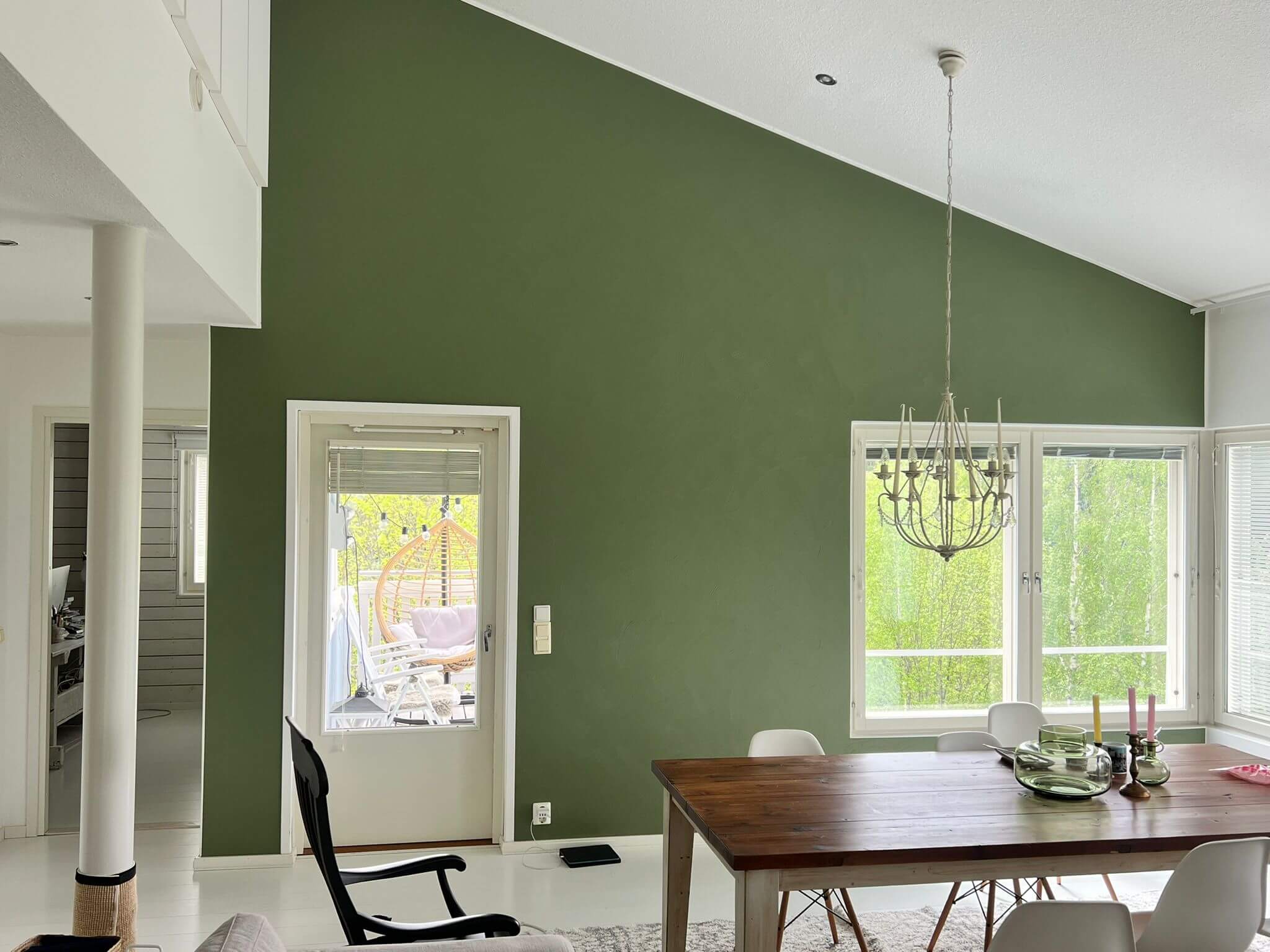 Sisätila, jossa on vihreä seinä, ruokapöytä ja tuoleja, sekä ikkuna ja ovi, valoisa ja avara.