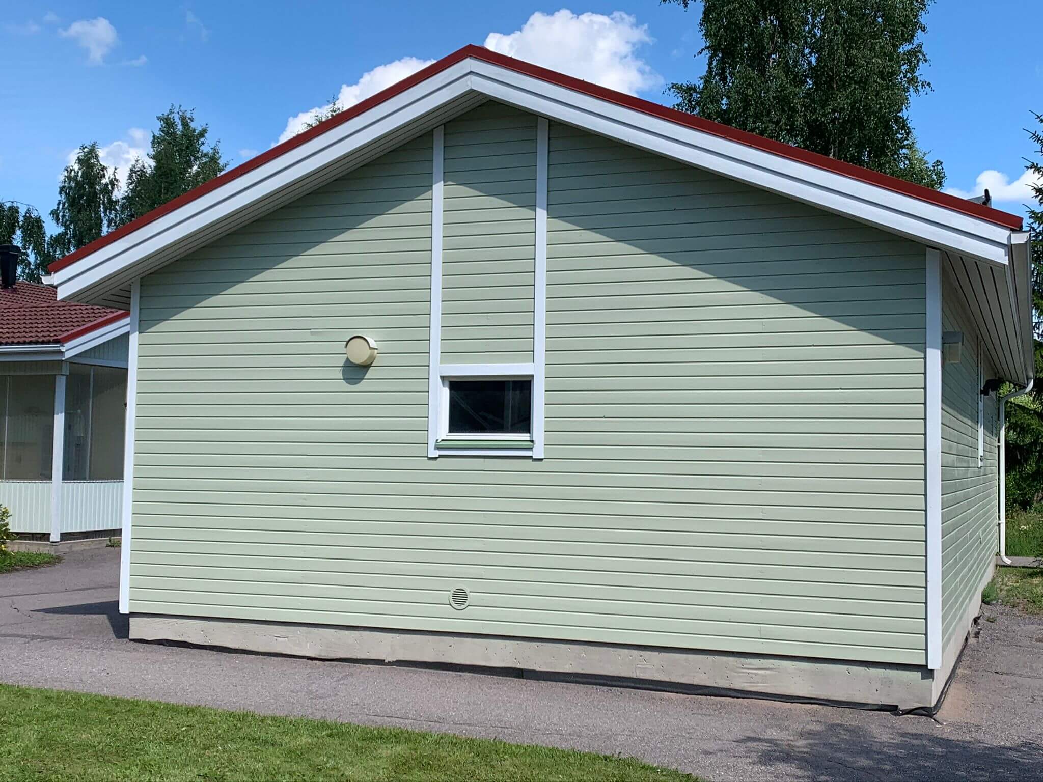 Vaaleanvihreä, yksikerroksinen rakennus punaisella katolla ja valkoisilla koristeilla aurinkoisena päivänä.