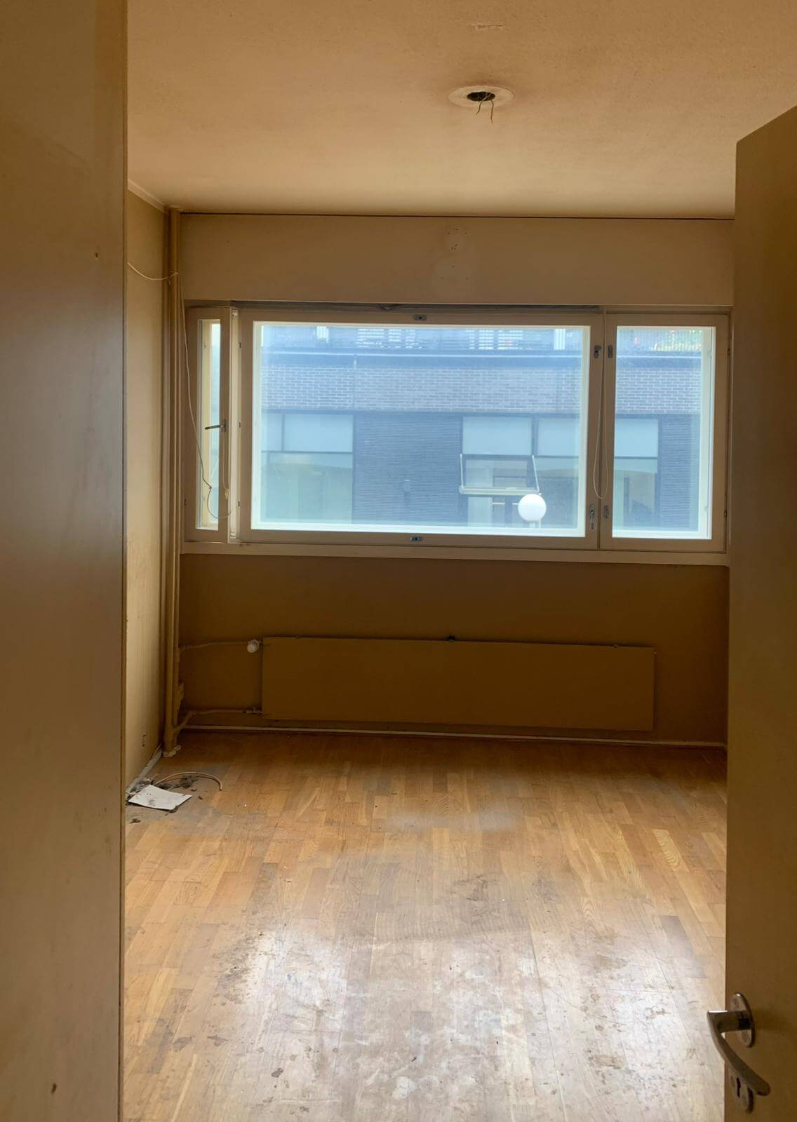 Tyhjä huone, jossa on puulattia, ikkuna ja lämpöpatteri.