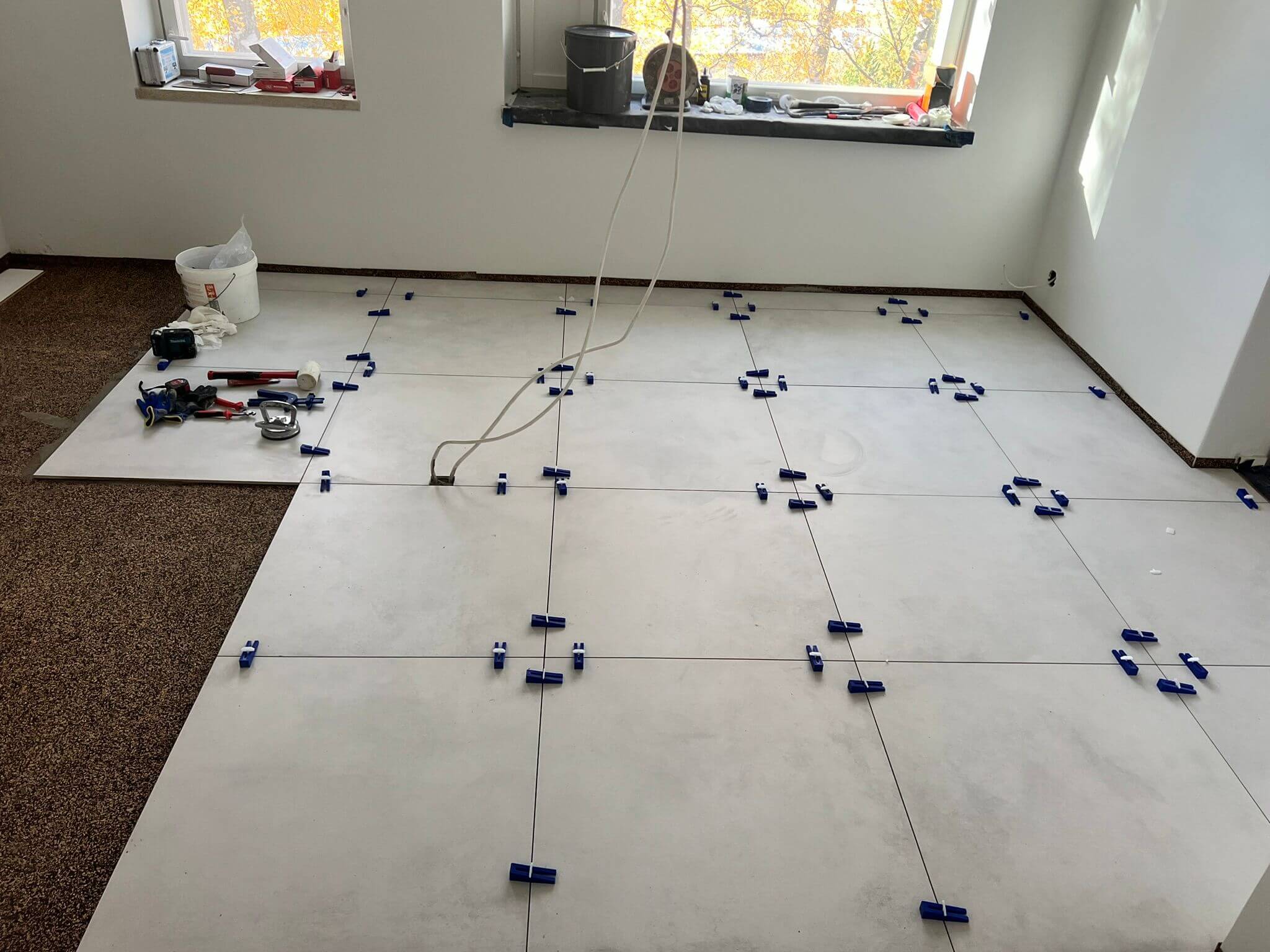 Huoneessa on lattialaatat, joissa on sinisiä kiiloja, ja ikkunalaudalla on työkaluja.