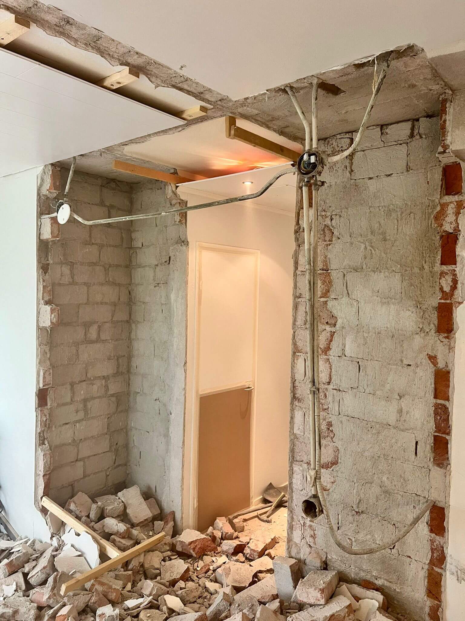 Keskeneräinen tiiliseinäaukko, jossa näkyy sähköjohdot, puupalkit ja tiiliskivikasat, valaistus on kirkas.