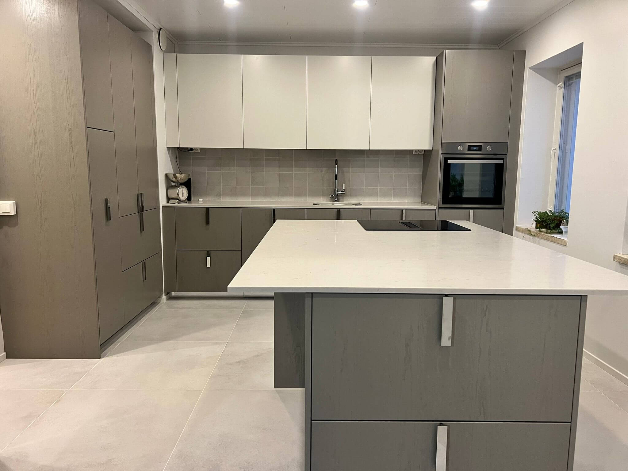 Moderni keittiö, jossa harmaat kaapit, valkoinen saareke ja laattalattia.