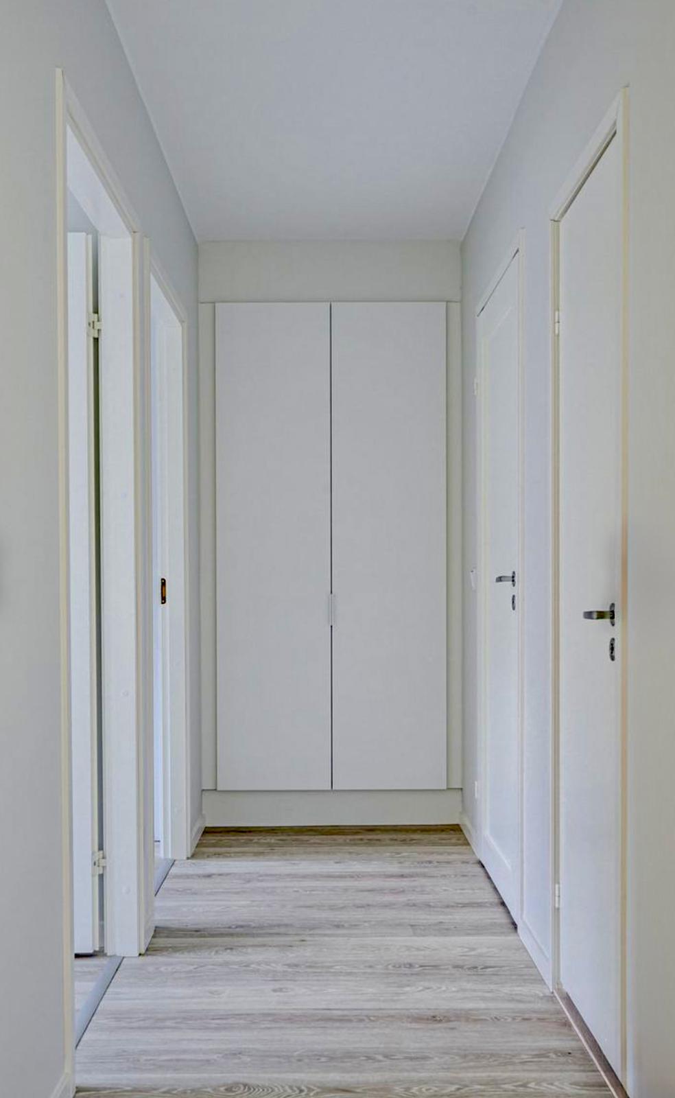 Vaalea käytävä, jossa on valkoiset ovet, vaatekaappi ja puulattia.