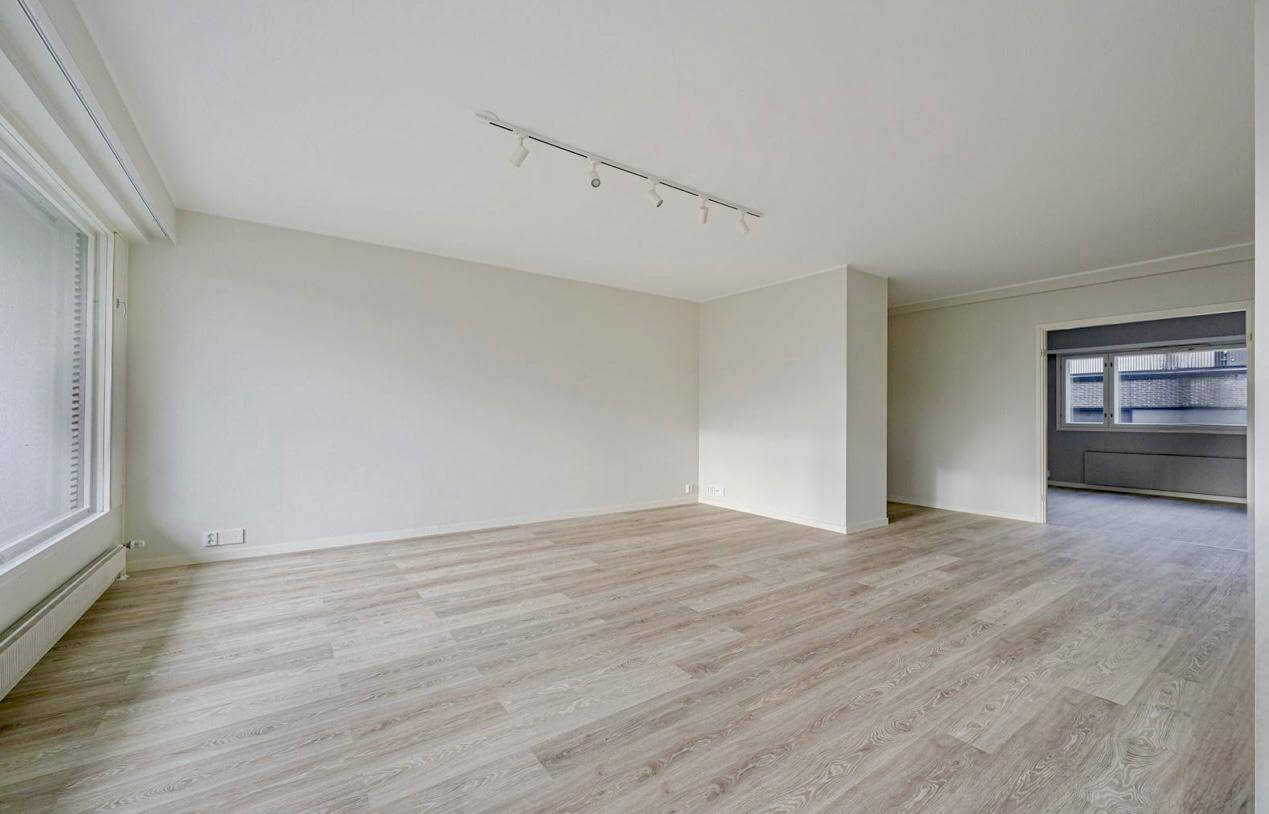 Tyhjä huone, jossa on puulattia, valkoiset seinät ja valaisimet katossa.