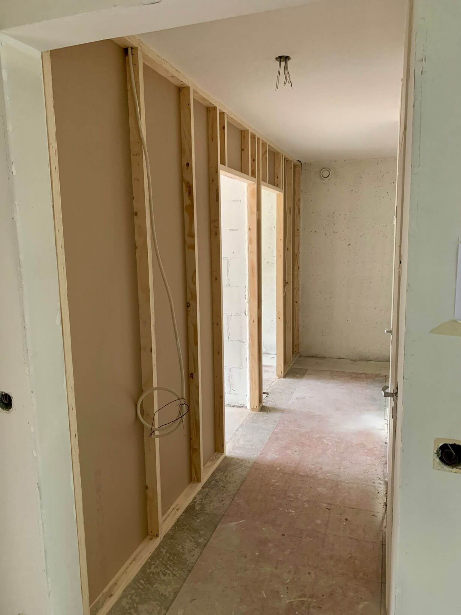 Rakenteilla oleva sisätila, jossa näkyy puurunkoja, johtoja ja keskeneräisiä seiniä, valaistus on kirkas ja luonnollinen.