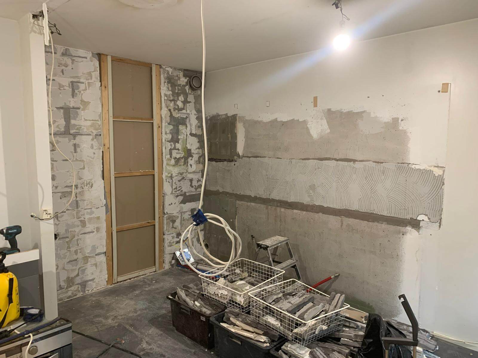 Huone remontin alla, jossa näkyy seinien purkutyöt, laattalaastin levitys ja laattakorit lattialla. Valoisa tila, jossa on keskeneräinen ilme.