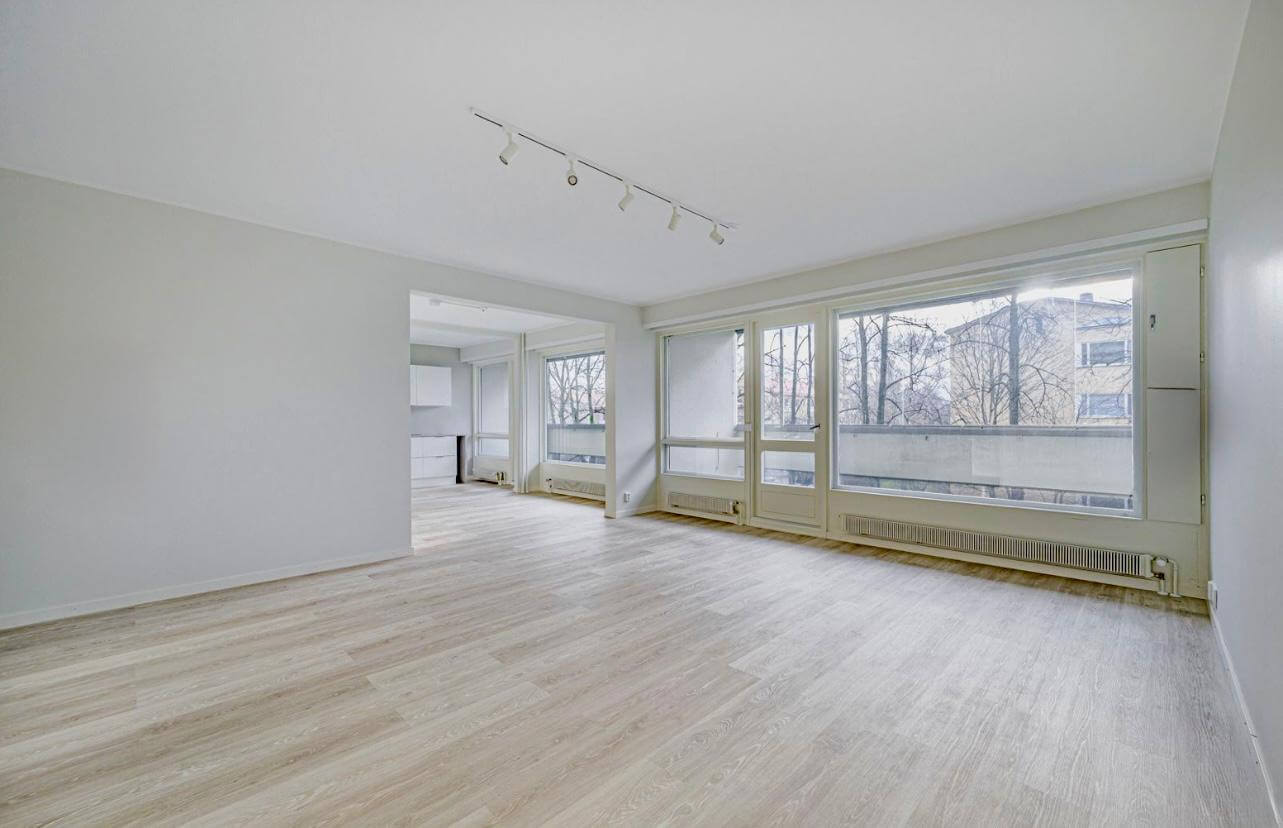 Vaalea, tyhjä huone, jossa on suuret ikkunat, vaalea puulattia ja valkoinen katto, jossa on kohdevalaisimet.