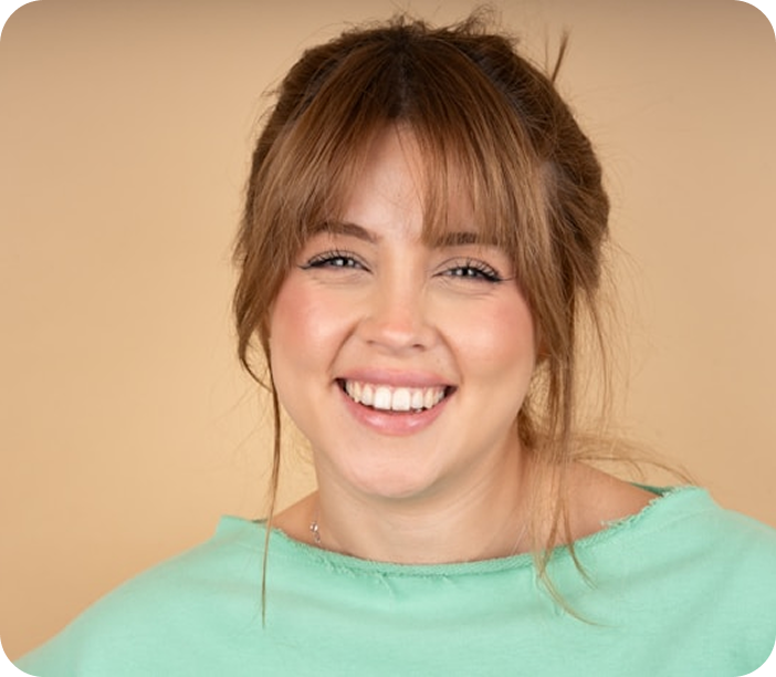 Smiling woman with light brown hair and bangs wearing a mint green shirt against a beige background.