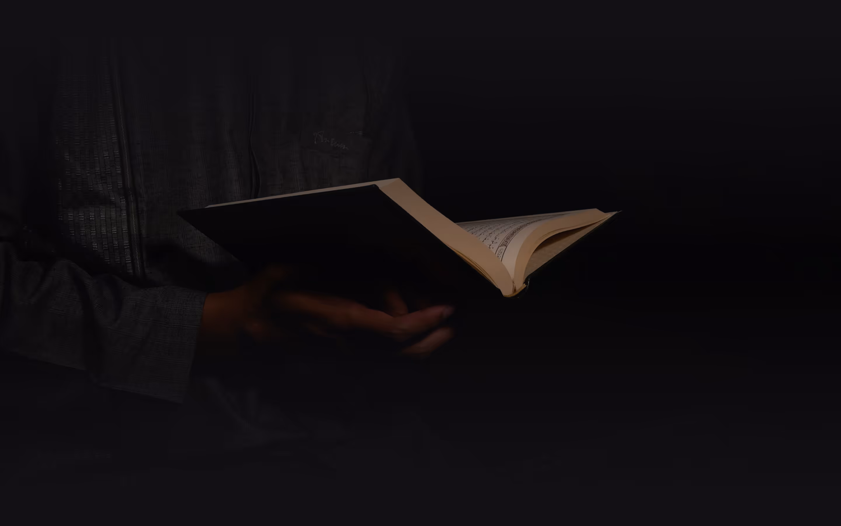 Person holding and reading an open book against a dark background.