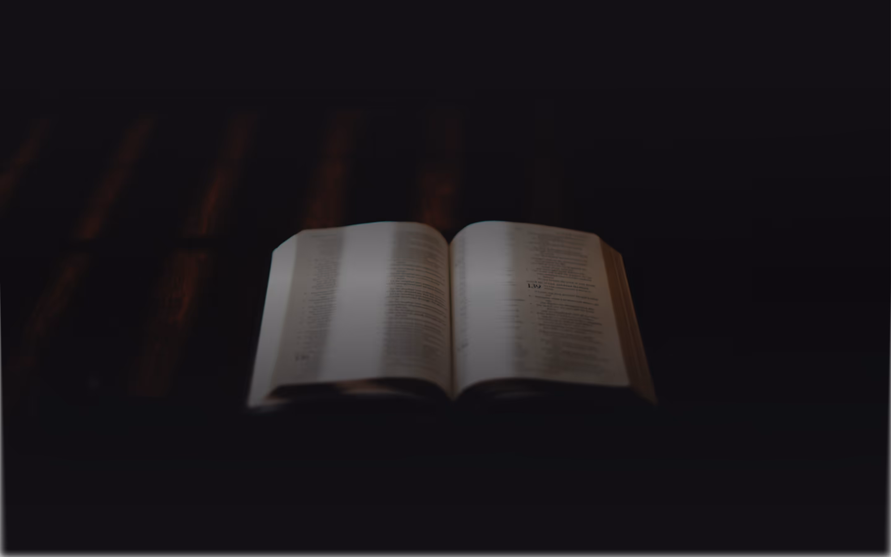 An open book illuminated in dim light, resting on a dark surface with blurred background.