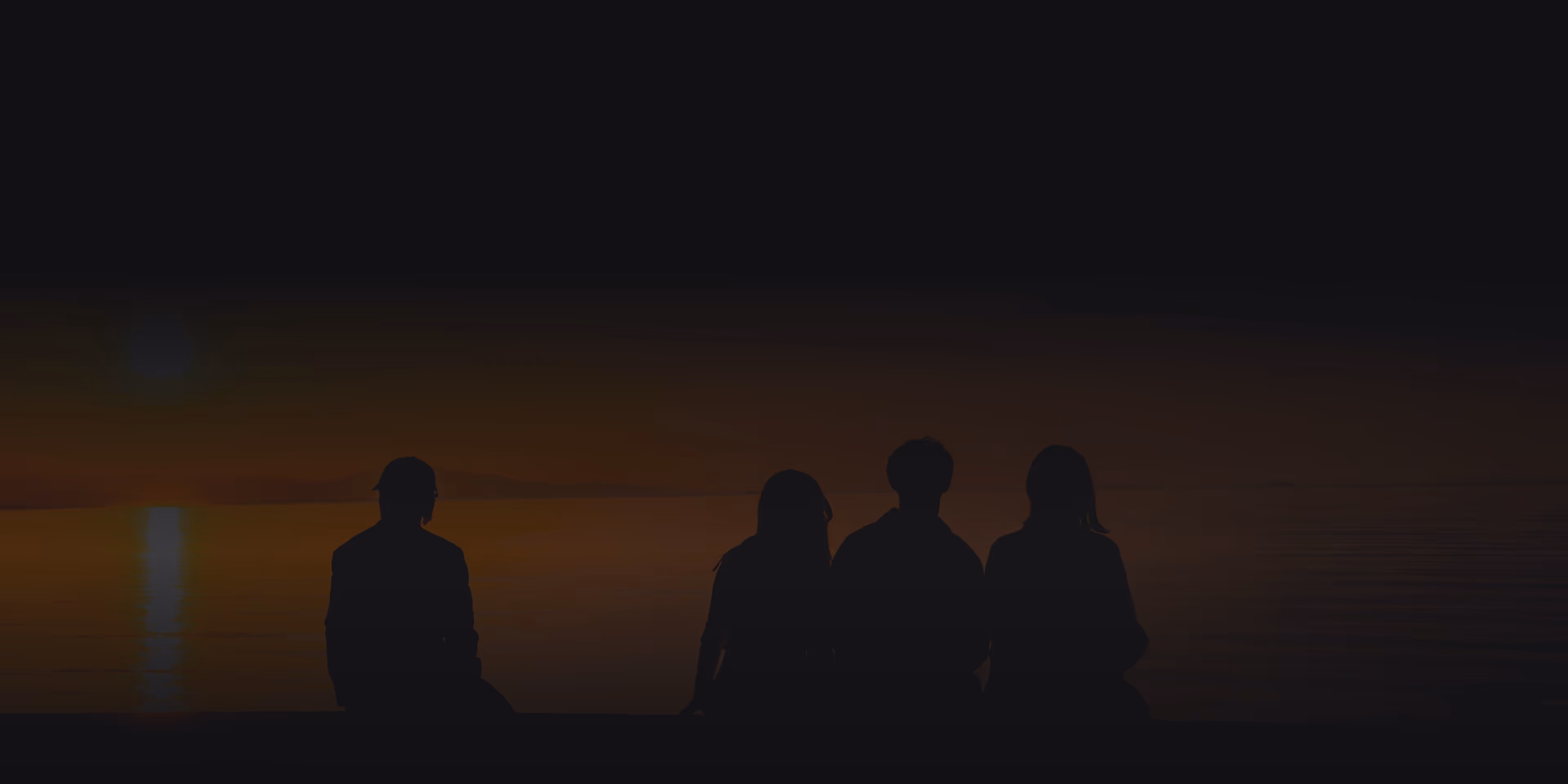 Silhouettes of four people sitting against a dark sunset sky over water, evoking a calm and reflective mood.