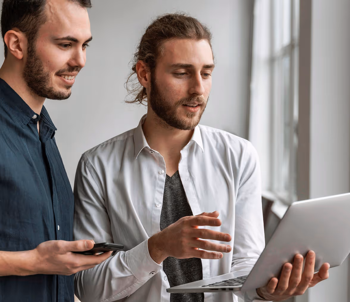 Two men looking at a laptop screen while one holds the laptop and the other holds a smartphone. - QuantumComp Webflow Template